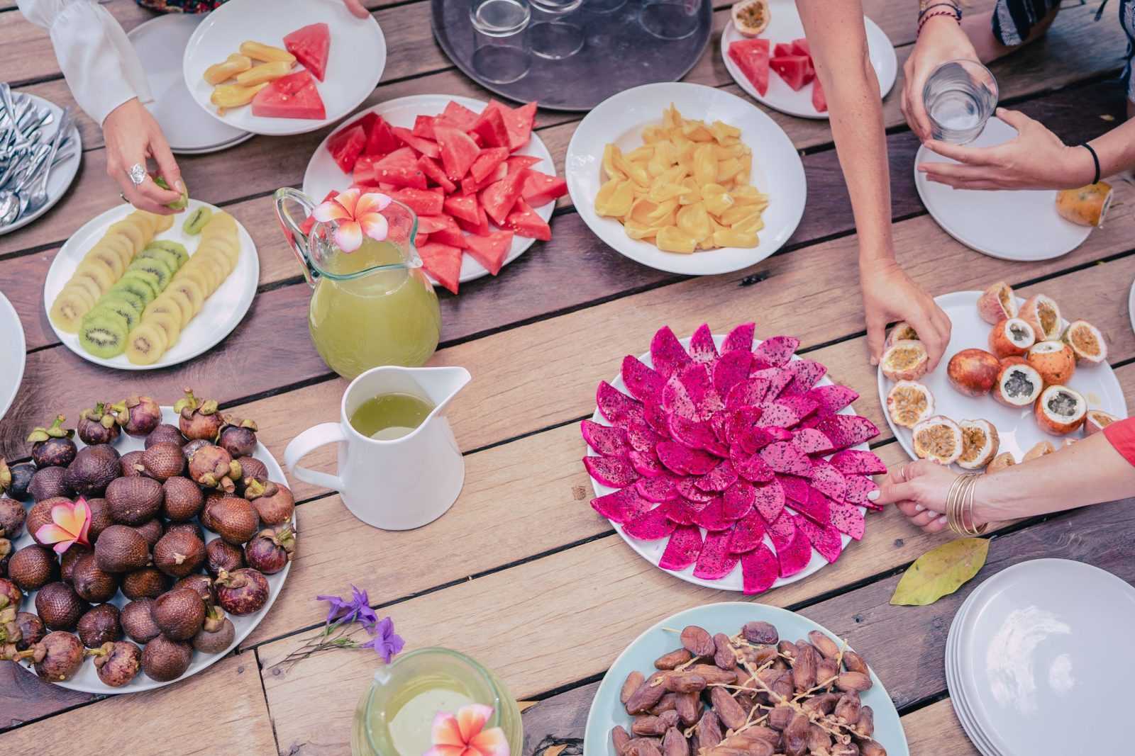 Platters of tropical fruit on a long wooden table at the women's workshop in Ubud, hands reaching in to serve