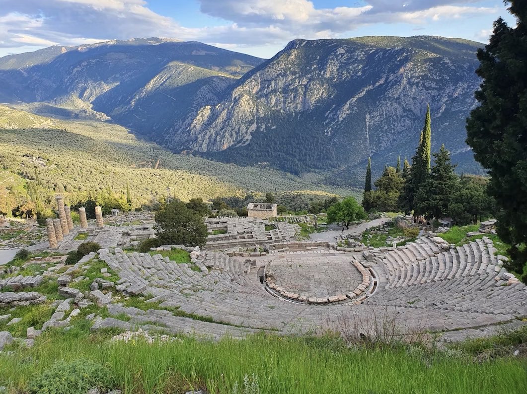 The ancient theatre at Delphi in Greece, stone tiers curving above the ruined temple of Apollo, with the mountains of Parnassus behind