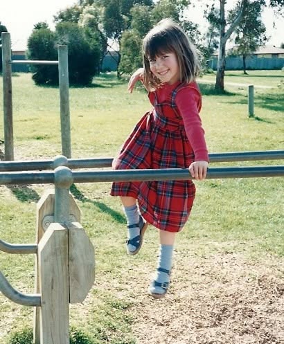 Jodie Louise as a small girl in a tartan dress climbing on playground bars