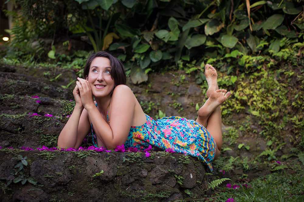 Jodie Louise lying on a mossy garden wall scattered with pink petals, looking up